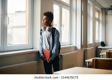 African American Elementary Student Thinking Of Something While Looking Through The Window In The Classroom. Copy Space. 