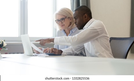 African american employee pointing at laptop discussing paperwork with colleague working together focused on computer task, black business employee helping giving online presentation to client