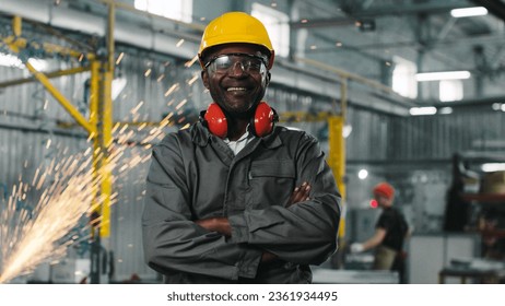 African american employee stared, smiling and posing for camera with crossed arms. Male engineer in googles and headphones at manufacture background where welding sparks flying. - Powered by Shutterstock