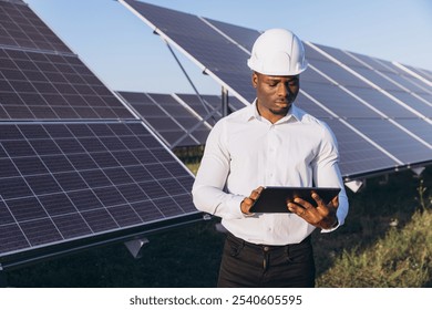 African American Engineer in a hard hat using a digital tablet to manage solar panels. Concept of renewable energy, technology, and sustainable development in a solar farm environment. - Powered by Shutterstock