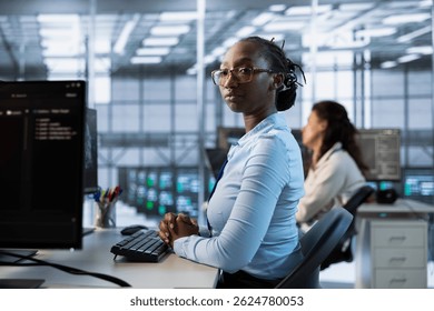 African american engineer managing and optimizing data center infrastructure for maximum efficiency and uptime. Woman in server room maintaining optimal system performance, performing backups