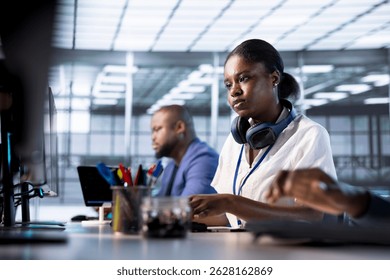 African american engineer next to coworkers in server farm checking recovery plan, monitoring data center energy consumption. Woman in server hub doing routine disk checks - Powered by Shutterstock - Get 15% off with code: PIKWIZARD15