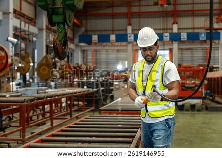 African American engineer worker is using the overhead crane hoist to carry raw materials in the metal sheet manufacturing factory for heavy industry