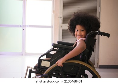 African - American ethnicity little girl resting on wheelchair while waiting to see the doctor in hospital. African - American girl sitting on a wheelchair and smiling to camera.