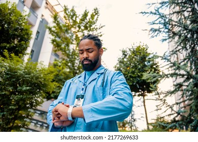 African American Ethnicity Male Doctor Late For His Shift In Hospital, Looking At His Hand Watch Outdoor. Man Nurse Checking The Time On Wristwatch Going To Work