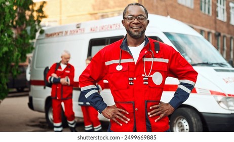 African American experienced adult doctor in red uniform standing in front of ambulance hospital car. Team of paramedics going to ambulance emergency call outdoors. Healthcare, first aid concept - Powered by Shutterstock