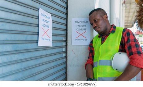 african american factory engineer at factory gate with annoucement of factory closed due to coronavirus covid-19 pandemic caused unemployment economics crisis and recession