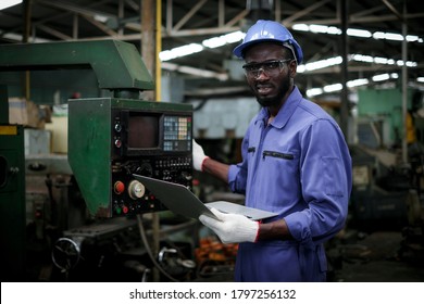 African American Factory Industrial Engineer Or Worker In Uniform Wear Safety Hardhat And Glasses Holding Laptop And Looking At Camera In Manufacturing Plant.maintenance And Industry Concept.