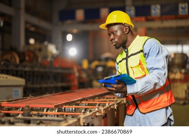 African american factory worker checking machinewith clipboard in metal sheet manufacture. supporting engineer, factory worker working in  management system for metal sheet factory, construction. - Powered by Shutterstock