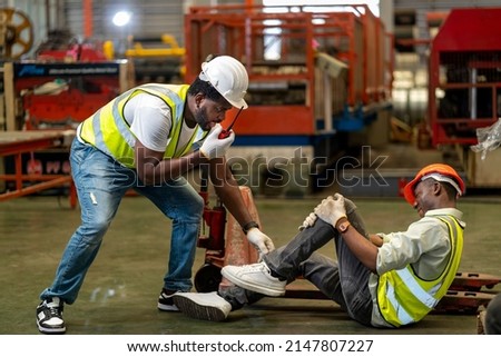 African American factory worker having accident while working in manufacturing site while his colleague is asking for first aid emergency team using walkie talkie radio for safety workplace usage