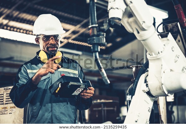 African American factory\
worker working with adept robotic arm in a workshop . Industry\
robot programming software for automated manufacturing technology\
.