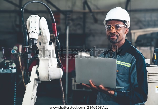 African American factory\
worker working with adept robotic arm in a workshop . Industry\
robot programming software for automated manufacturing technology\
.