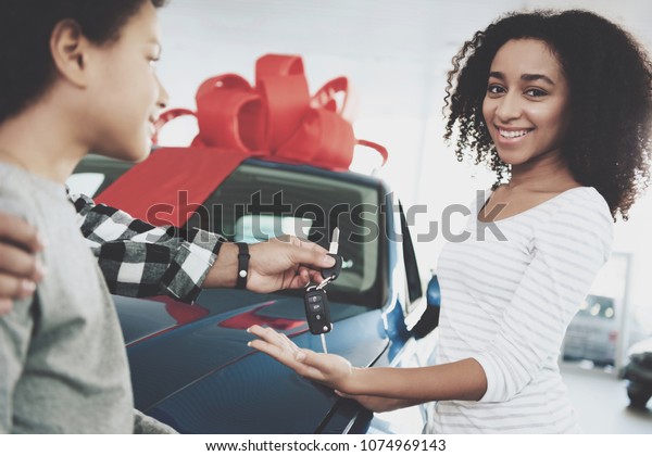 African\
american family at car dealership. Father, mother and son near new\
blue car. Man is presenting keys to\
woman.