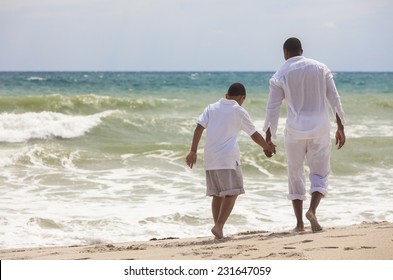 African American family of father and son, man & boy child, walking, holding hands and having fun in the sand and waves on a sunny beach