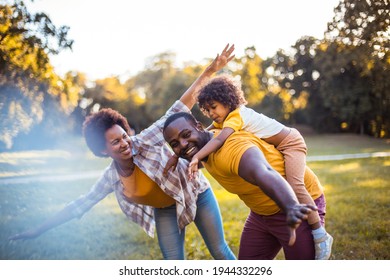 African American Family Having Fun Outdoors. Father Carrying Daughter On Piggyback. 