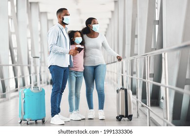 African American Family In Medical Masks Standing In Airport Terminal, Holding Suitcases, Passports And Tickets, Looking At Window, Waiting For Departure, Travelling Together During Covid Pandemic