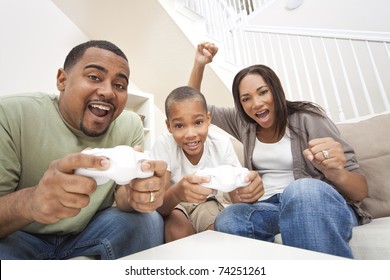 African American family, parents and son, having fun playing computer console games together, Father and son have the handset controllers and the mother is cheering the players.