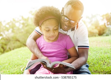 African American Family Reading A Book Together In The Outdoor Park