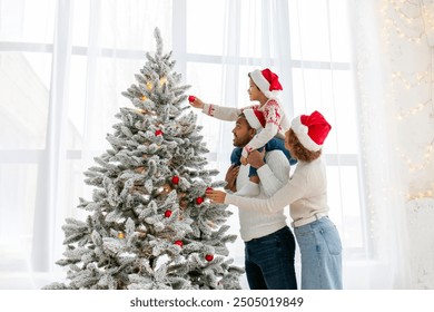 African American family in Santa hat celebrate New Year together at home and decorate Christmas tree, teenage boy celebrates New Year with mom and dad and holds red toy - Powered by Shutterstock