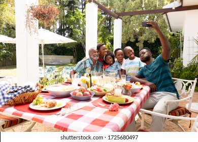 African American family spending time together in the garden on a sunny day, sitting by a table and having a lunch, while a man is taking a selfie with his smartphone.  - Powered by Shutterstock