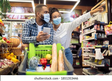 African American Family At Supermarket. Black Couple Buying Food Doing Grocery Shopping Together Using Phone App Walking With Cart In Groceries Shop. Happy Buyers In Store Searching Sales Concept