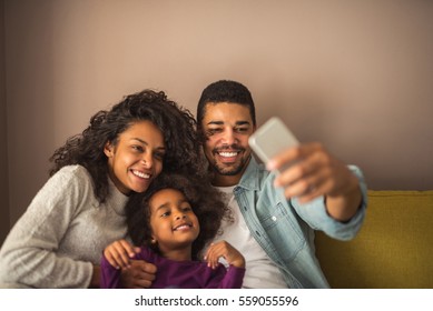 African American Family Taking Pictures With Mobile Phone At Home.