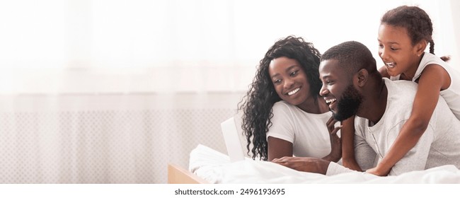 African american family of three using laptop while lying on bed together, browsing internet or watching movie - Powered by Shutterstock