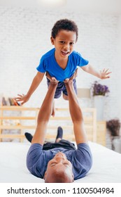 African American family of two, father lifting son up high on bed at home