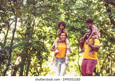 African American family walking trough park. Parents carrying children on piggyback. - Powered by Shutterstock