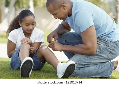 African American father applying bandaid to daughter outdoors