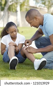 African American Father Applying Bandaid To Daughter Outdoors