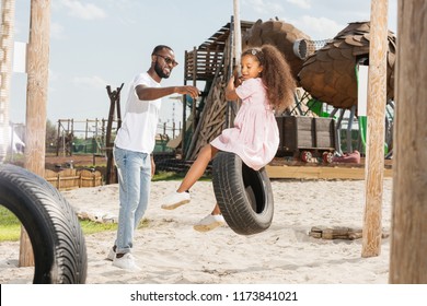 African American Father Catching Daughter On Tire Swing At Amusement Park