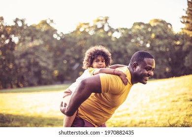 African American Father And Daughter Having Fun Outdoors. Father Carrying Daughter On Piggyback.