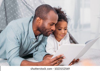 African American Father And Daughter Lying On Floor And Reading Together At Home