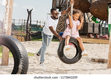 African American Father And Daughter On Tire Swing Having Fun On Playground