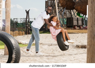 African American Father And Daughter On Tire Swing At Amusement Park