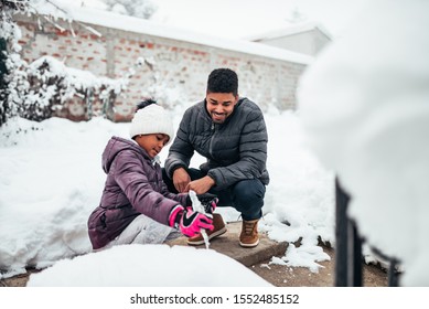 African American Father And Daughter Playing In The Snow In The Backyard.