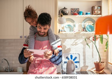 African American Father And Daughter Reading A Recipe In The Kitchen. They Are Both Happy. 