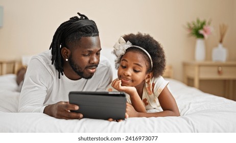 African american father and daughter watching video on touchpad lying on bed at bedroom - Powered by Shutterstock