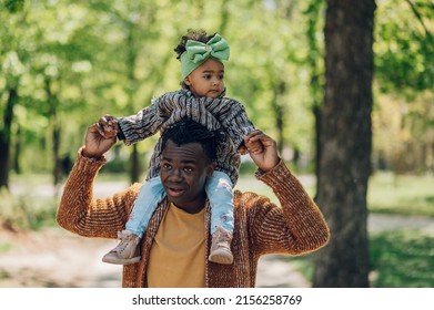 African American Father And His Cute Daughter Playing And Bonding In The Park. Leisure Recreation Lifestyle. Enjoying Active Weekend. Dad Holding His Daughter On His Shoulders.