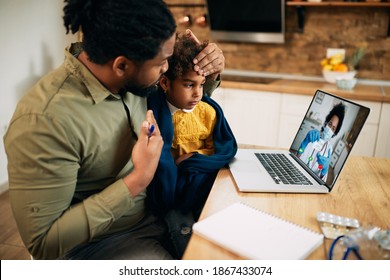 African American Father And His Sick Daughter Using Laptop While Having Video Call With Family Doctor During Coronavirus Pandemic. Focus Is On Daughter. 