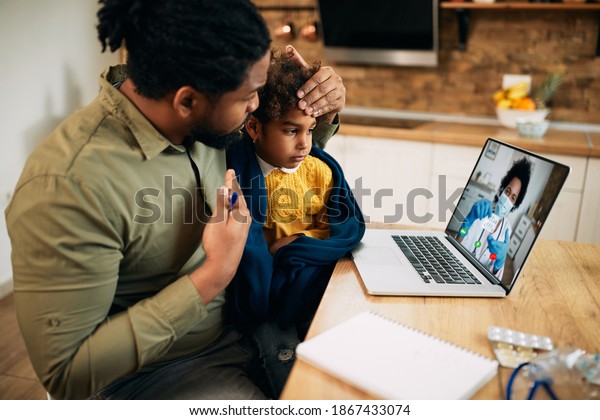 African American father and his sick\
daughter using laptop while having video call with family doctor\
during coronavirus pandemic. Focus is on daughter.\

