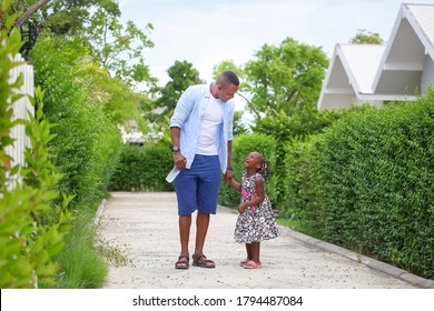 African American Father Is Holding His Happy Little Daughter Hand And Having A Good Time Together While Walking Outside The House Around The Neighborhood During Summer Time