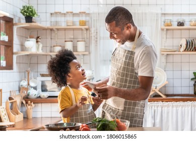 African American Father And Little Son Playing And Laughing During Cooking In Kitchen. Black Family Having Fun Preparing Healthy Food Together At Home. Brazilian Single Dad And Boy With Smiling Face