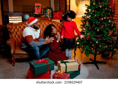 African American father and mother clap hands to cheer their daughter dance near Chritmas tree and enjoy together at home during night time.