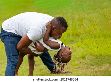 African American Father Playing With Young Happy Little Daughter On Green Grass Field While Enjoying Summer Garden Outdoor In The Neighborhood With Copy Space