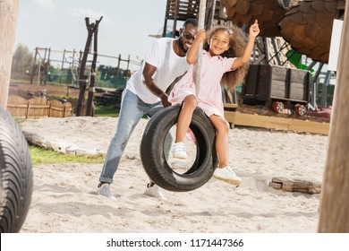 African American Father Pushing Daughter On Tire Swing At Amusement Park