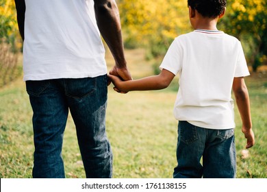 African American Father And Son Holding Hands In The Outdoor Park During Summertime. Fatherhood And Happy Family Time Together Concept