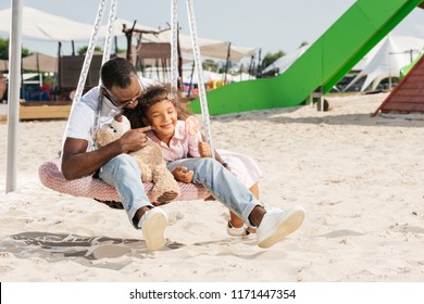 African American Father Touching Daughter Cheek On Spider Web Nest Swing At Amusement Park