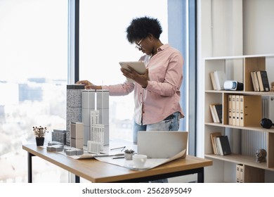 African American female architect in office develops modern city project using digital tablet. Urban planning and innovation highlighted as she focuses on model. - Powered by Shutterstock - Get 15% off with code: PIKWIZARD15